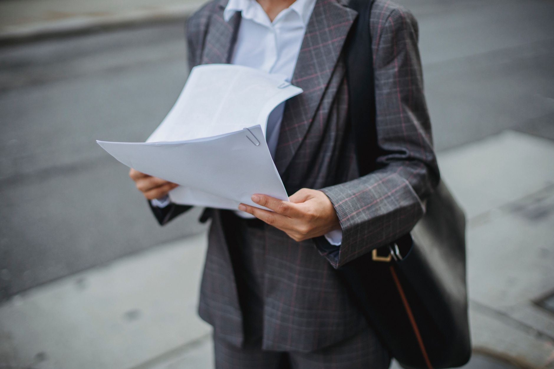 Ilustrasi: Professional businesswoman reviewing documents outdoors in a city environment.