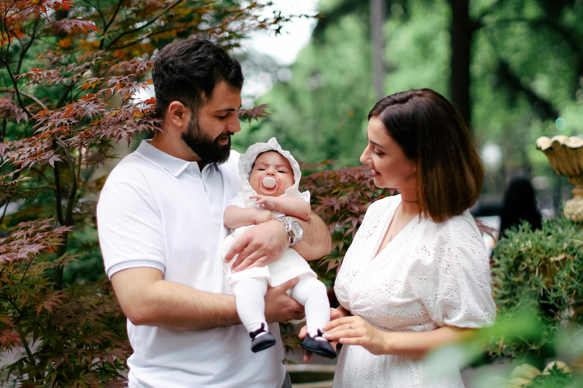 Ilustrasi: A joyful family scene featuring parents holding their newborn baby outdoors, capturing a loving moment.