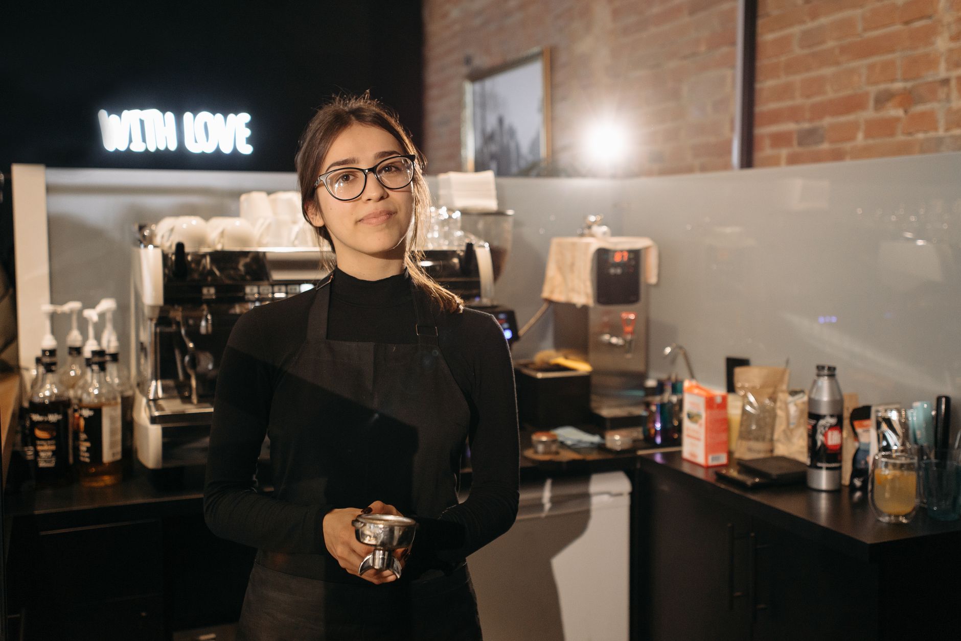 Ilustrasi: Smiling barista holding portafilter inside a cozy cafe with coffee machine, wearing apron and glasses.
