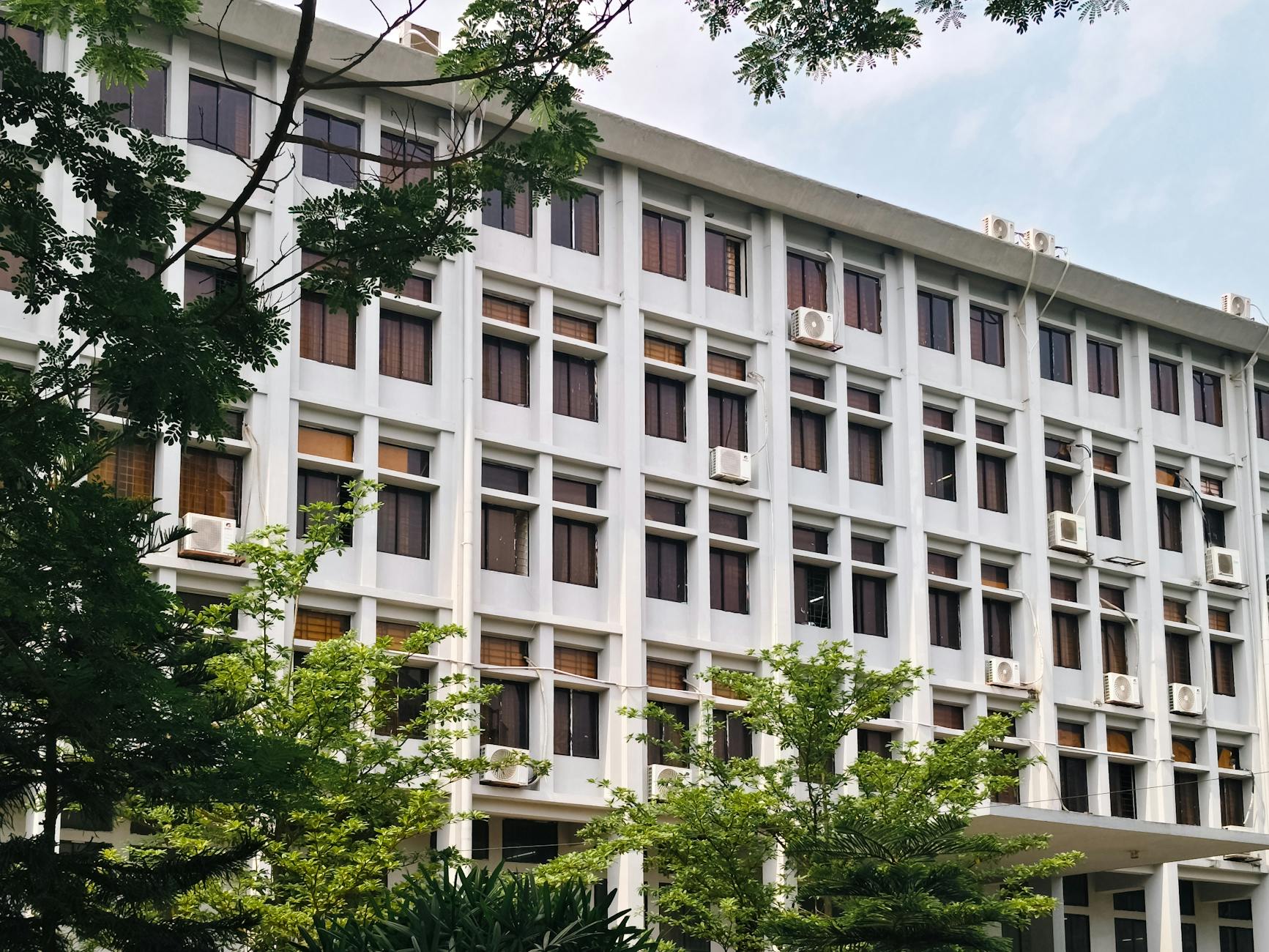 Ilustrasi: A modern office building exterior with air conditioners and lush green trees.