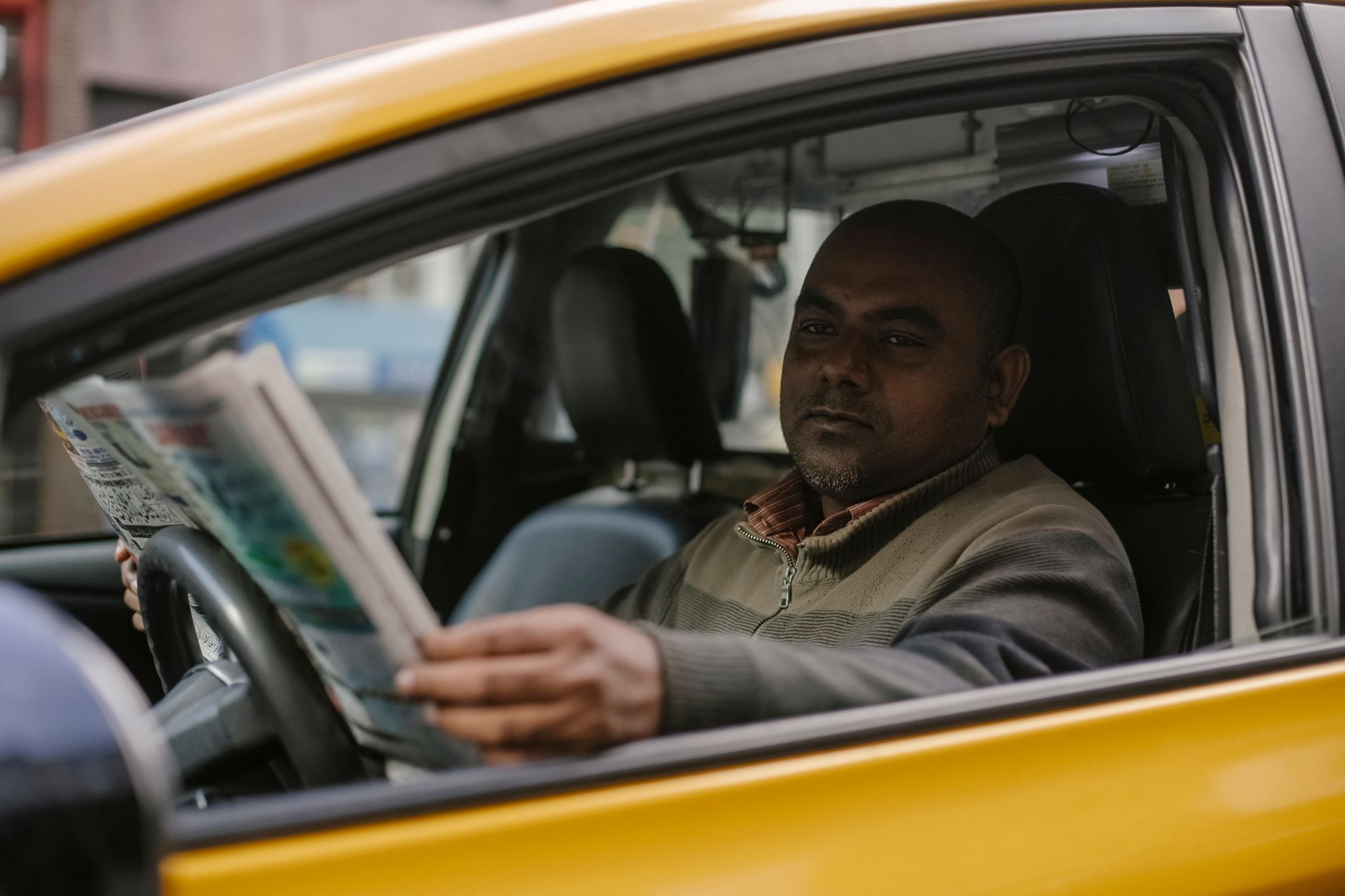 Ilustrasi: Concentrated ethnic male driver sitting at steering wheel and reading magazine while waiting for client