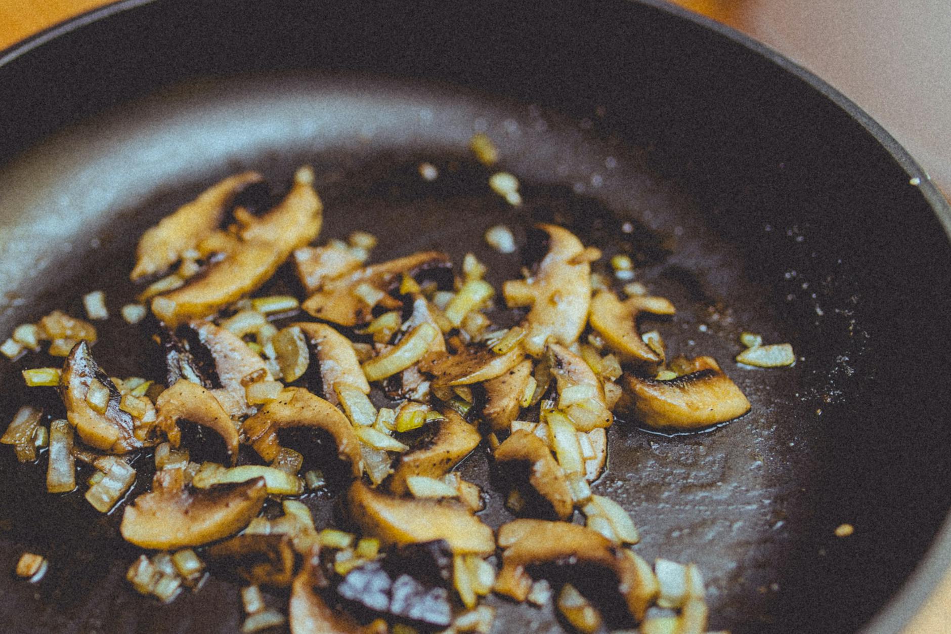Ilustrasi: Close-up of sliced mushrooms and onions sautéing in a skillet, showcasing cooking detail.