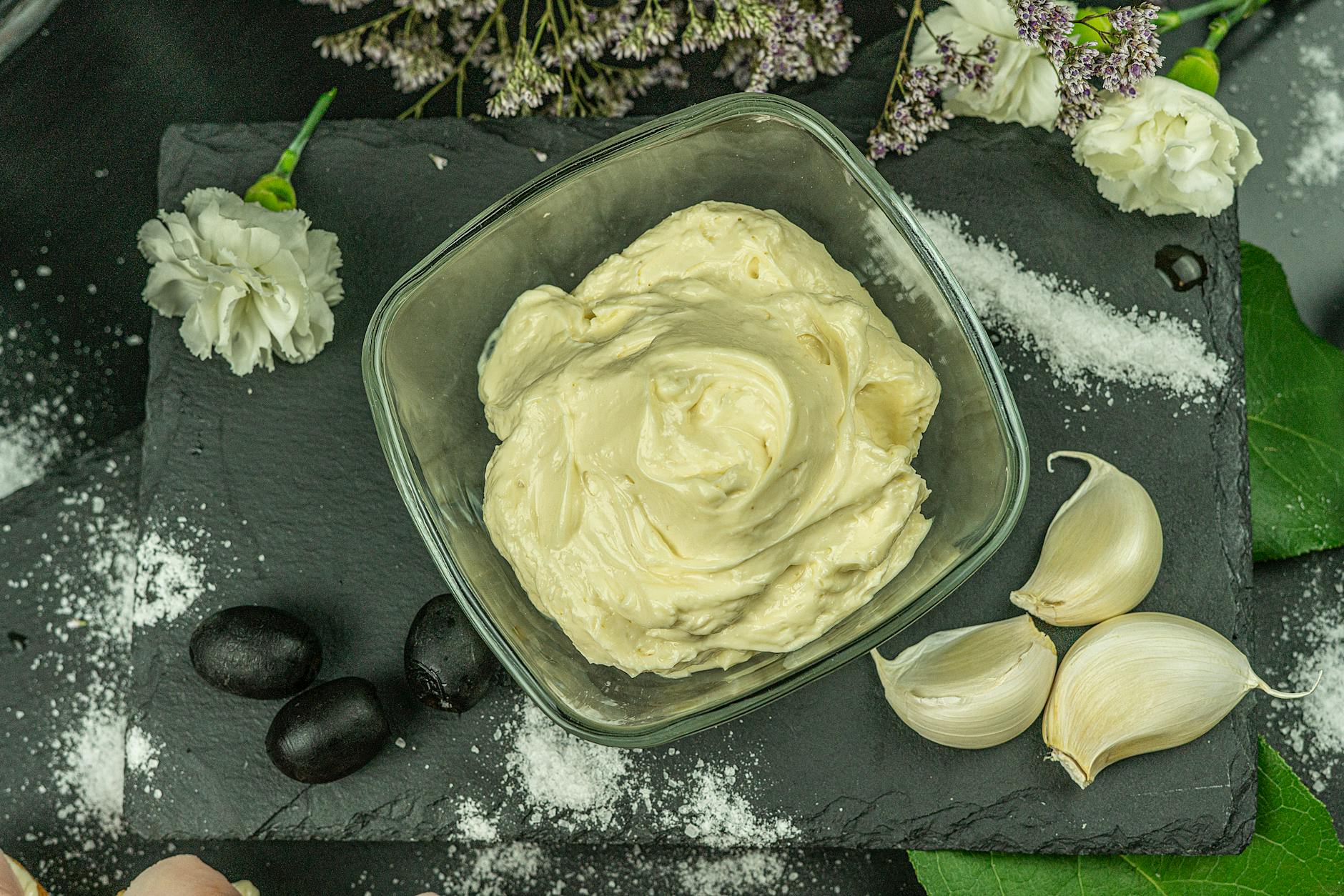 Ilustrasi: A creamy white sauce elegantly presented with garlic and olives on a slate board.