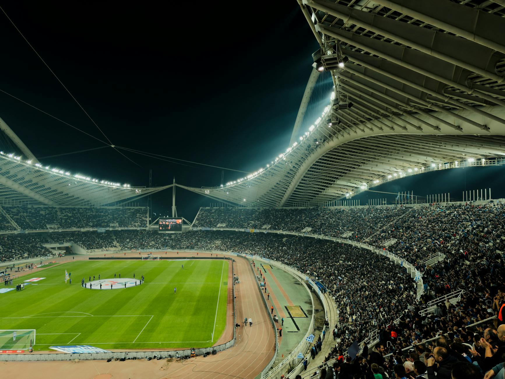 Ilustrasi: A crowded sepak bola stadion under bright lights malam hari, capturing the excitement of a live sports event.