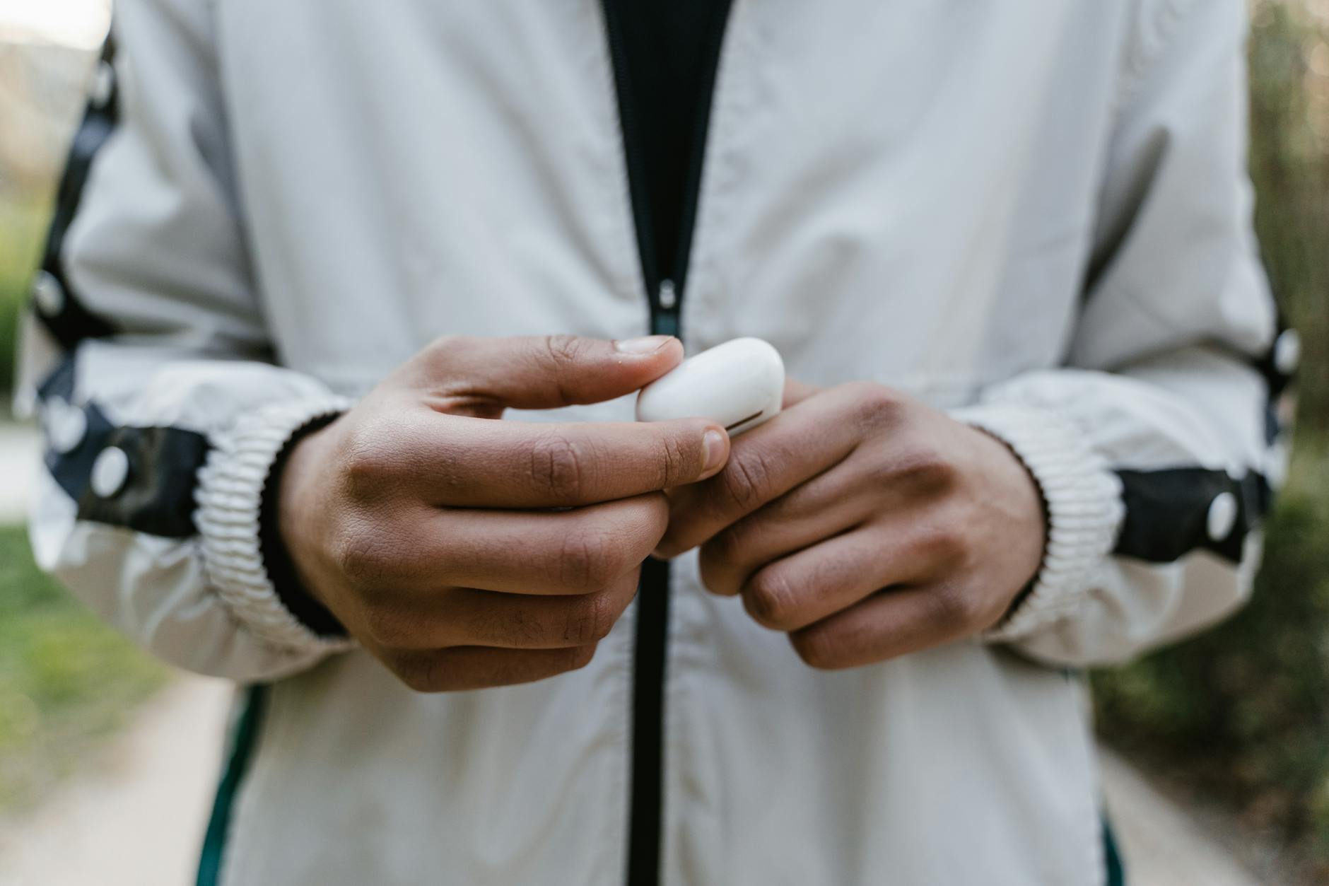 Ilustrasi: A person in a jacket holding a case of wireless earbuds outdoors.