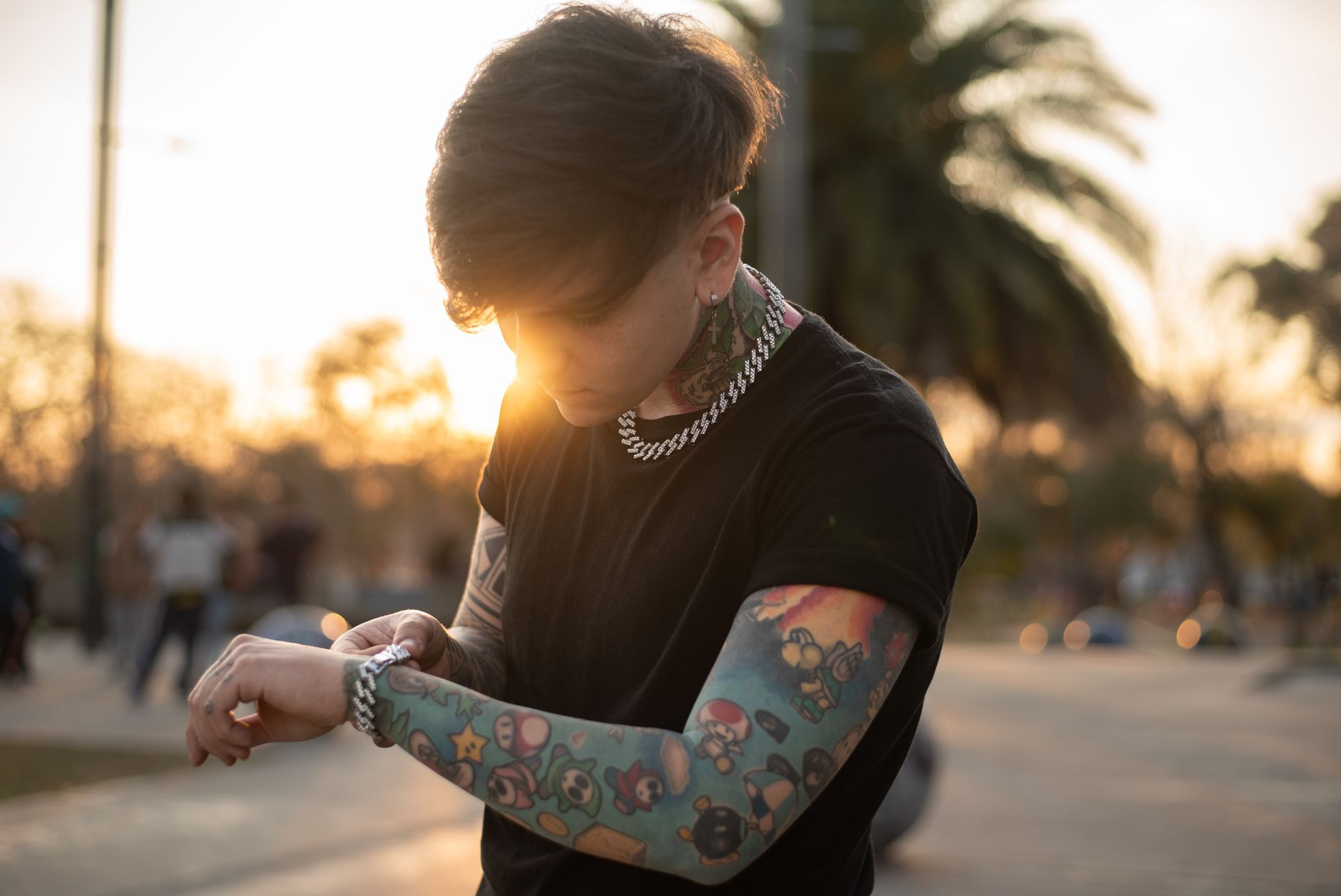 Ilustrasi: A tattooed person wearing a black shirt checks a smartwatch outdoors at sunset.